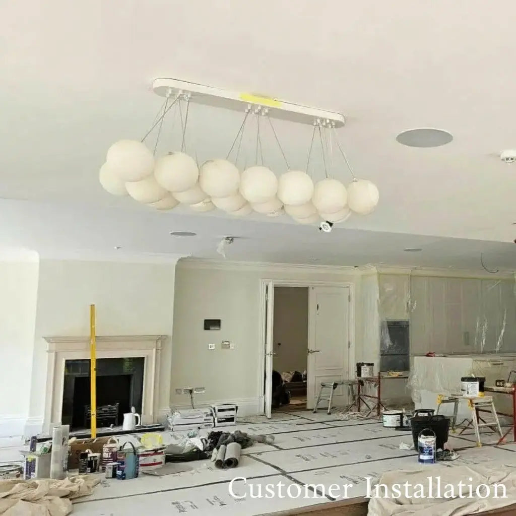 Modern chandelier hanging in a room under construction with visible tools and materials on the floor.