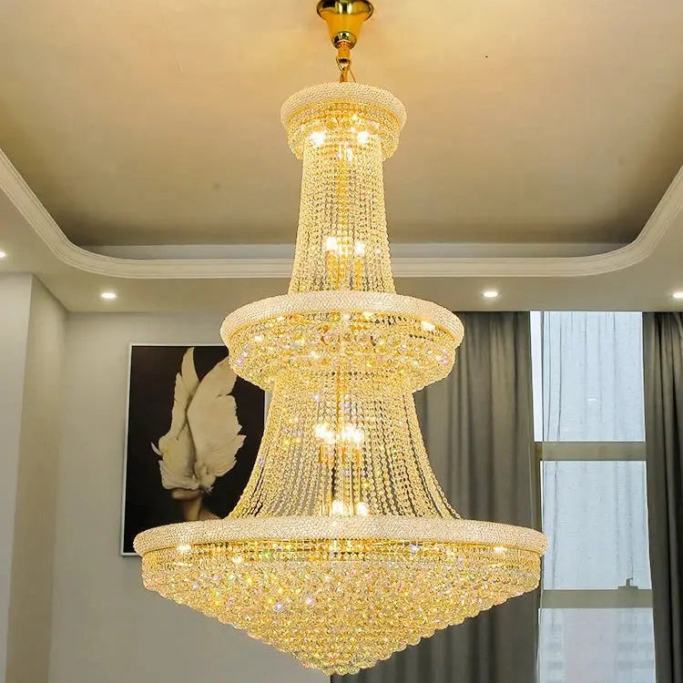 Gold chandelier hanging in a room with a window and wall decor.